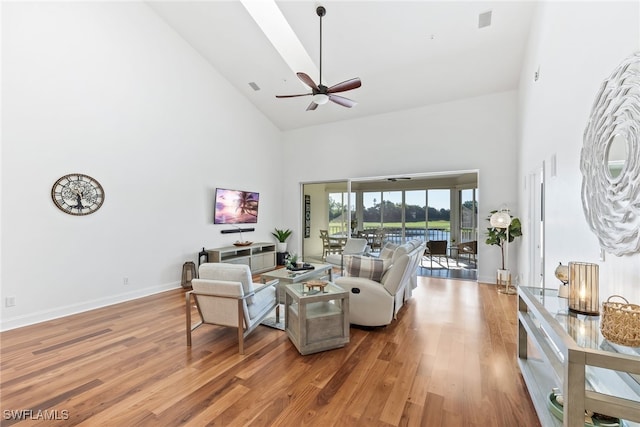 living room featuring a ceiling fan, visible vents, baseboards, light wood-style flooring, and a high ceiling