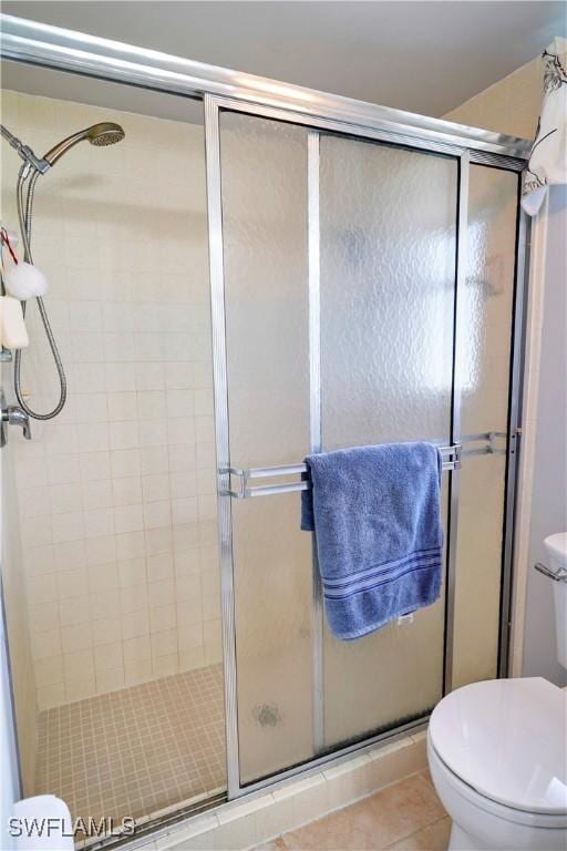 bathroom featuring tile patterned flooring, toilet, and a shower with shower door