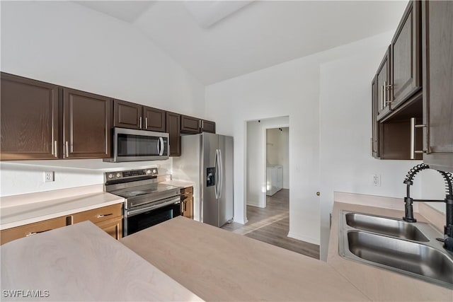 kitchen featuring sink, stainless steel appliances, high vaulted ceiling, dark brown cabinetry, and light wood-type flooring