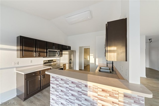 kitchen with sink, kitchen peninsula, stainless steel appliances, dark brown cabinets, and light hardwood / wood-style flooring