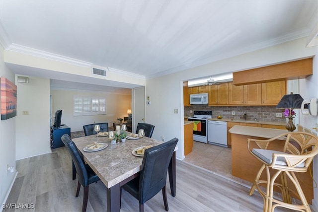 dining space with ornamental molding, sink, and light wood-type flooring