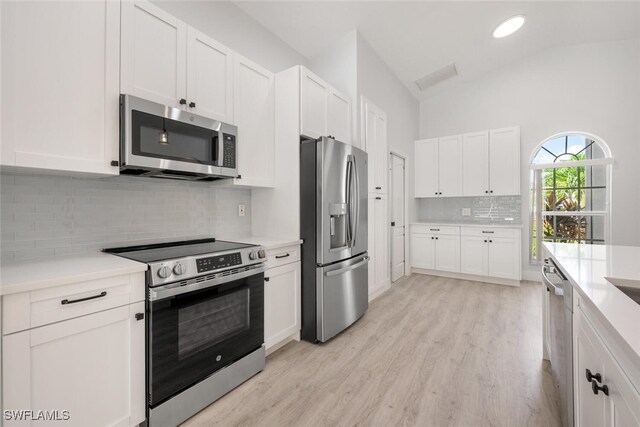 kitchen featuring white cabinetry, light hardwood / wood-style flooring, appliances with stainless steel finishes, decorative backsplash, and vaulted ceiling