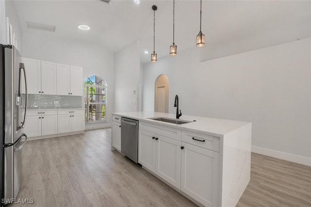 kitchen with arched walkways, a sink, appliances with stainless steel finishes, light wood-type flooring, and decorative backsplash