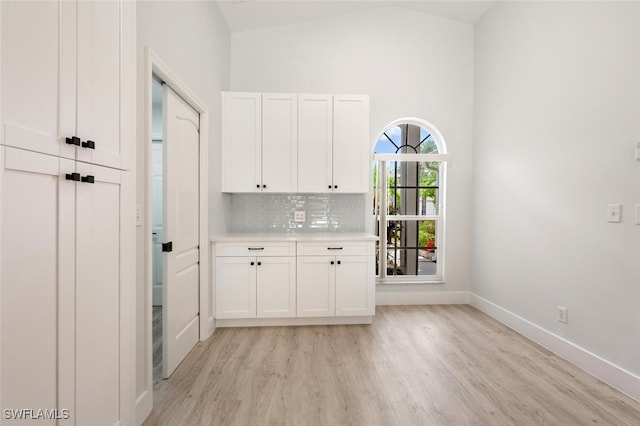 interior space with high vaulted ceiling, white cabinets, decorative backsplash, and light wood-type flooring