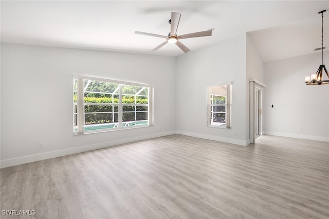 empty room with ceiling fan with notable chandelier, light hardwood / wood-style flooring, and vaulted ceiling