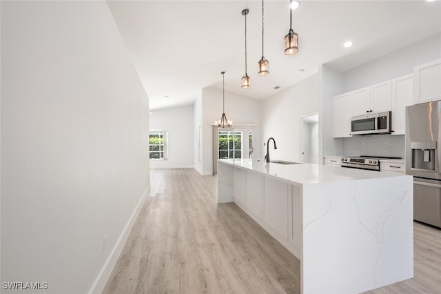 kitchen with stainless steel appliances, hanging light fixtures, sink, light stone counters, and light hardwood / wood-style floors