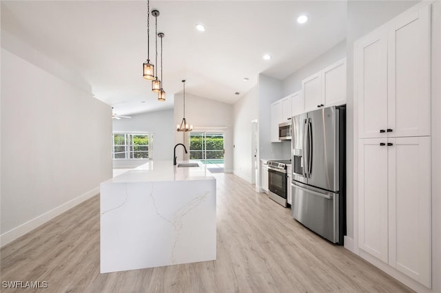 kitchen featuring appliances with stainless steel finishes, light hardwood / wood-style flooring, vaulted ceiling, hanging light fixtures, and white cabinetry