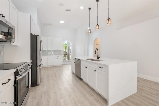 kitchen with light wood-type flooring, an island with sink, stainless steel appliances, hanging light fixtures, and sink