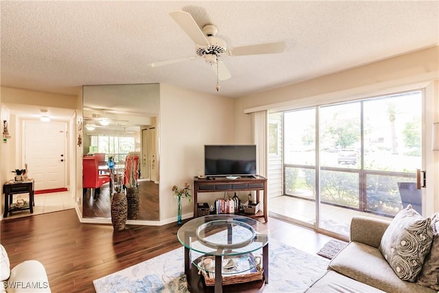 living area with ceiling fan, plenty of natural light, wood finished floors, a textured ceiling, and baseboards