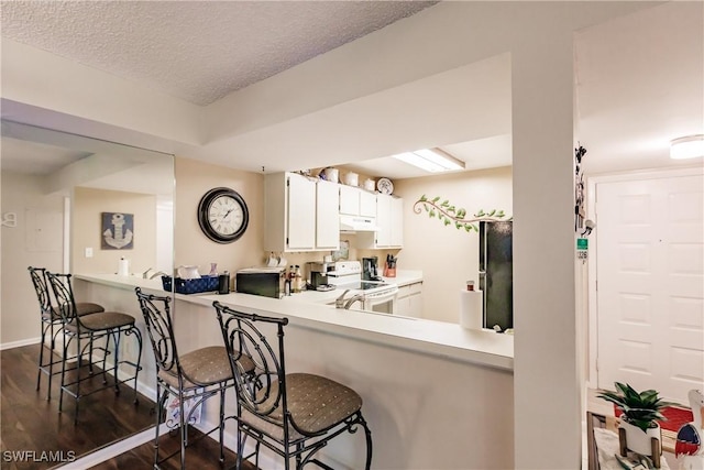 kitchen with electric stove, dark wood finished floors, freestanding refrigerator, light countertops, and a kitchen bar