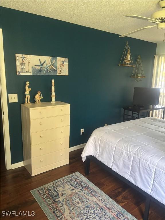 bedroom with a textured ceiling, baseboards, dark wood-style flooring, and ceiling fan
