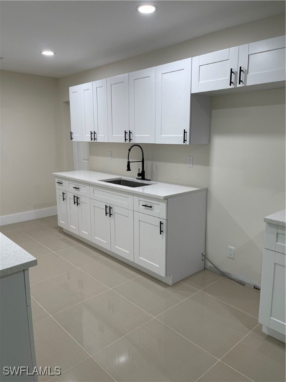 kitchen with light tile patterned flooring, sink, white cabinets, and light stone countertops