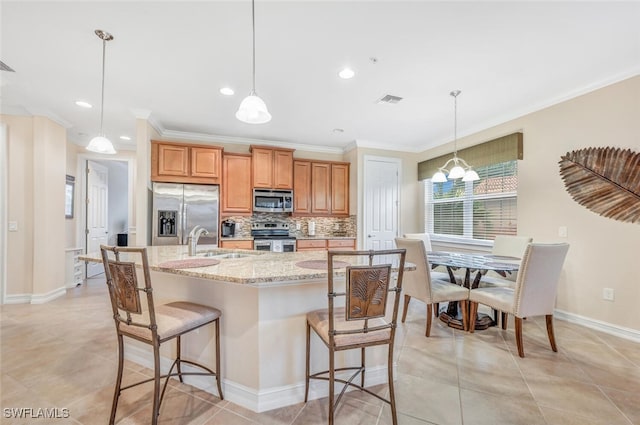 kitchen with sink, hanging light fixtures, stainless steel appliances, light stone counters, and a spacious island