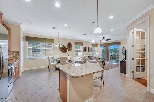 kitchen with sink, an island with sink, hanging light fixtures, and ceiling fan with notable chandelier