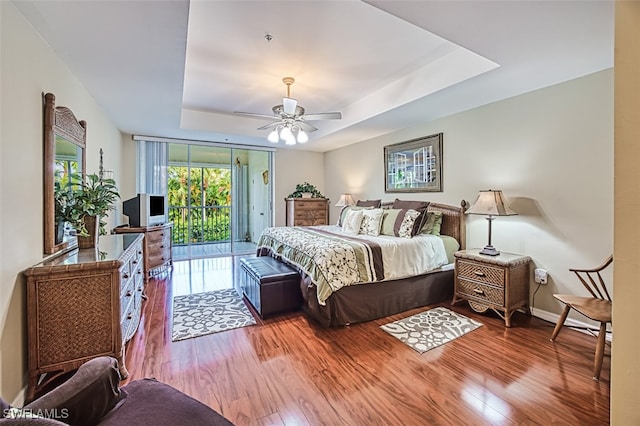 bedroom with ceiling fan, access to outside, hardwood / wood-style floors, and a tray ceiling