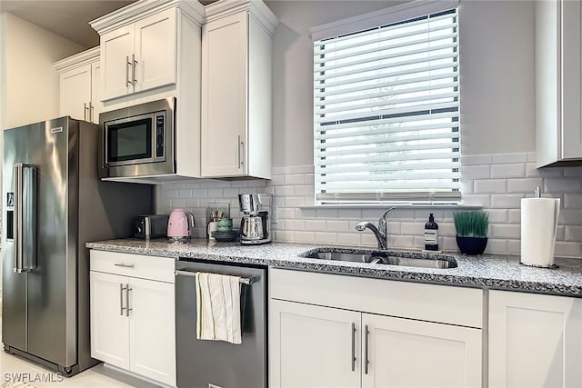 kitchen featuring white cabinets, light stone countertops, appliances with stainless steel finishes, decorative backsplash, and sink