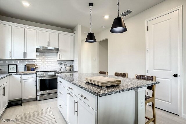 kitchen featuring stainless steel stove, tasteful backsplash, white cabinets, light stone counters, and a kitchen island