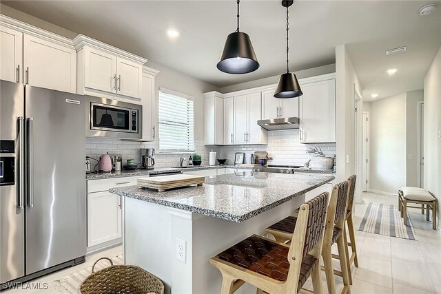 kitchen with tasteful backsplash, light tile patterned floors, white cabinets, stainless steel appliances, and light stone countertops