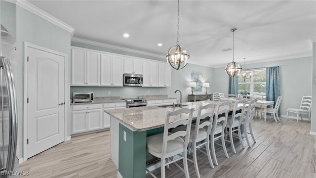 kitchen featuring white cabinets, light stone countertops, an island with sink, stainless steel appliances, and sink