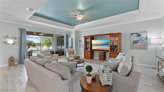 living room with ceiling fan, ornamental molding, light hardwood / wood-style floors, and a tray ceiling