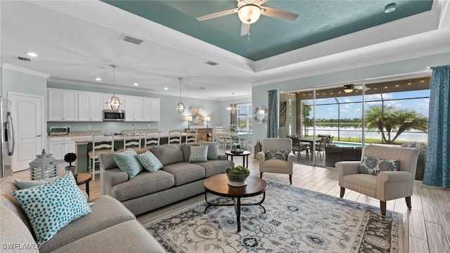 living room featuring light hardwood / wood-style flooring, ceiling fan with notable chandelier, ornamental molding, and a raised ceiling