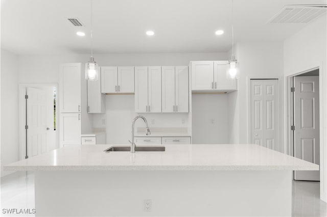 kitchen with a center island with sink, hanging light fixtures, sink, and white cabinets