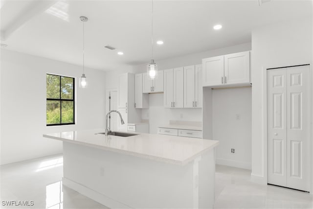 kitchen featuring decorative light fixtures, white cabinets, a kitchen island with sink, and sink