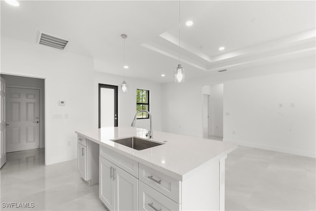 kitchen with a center island with sink, hanging light fixtures, sink, white cabinetry, and light stone counters