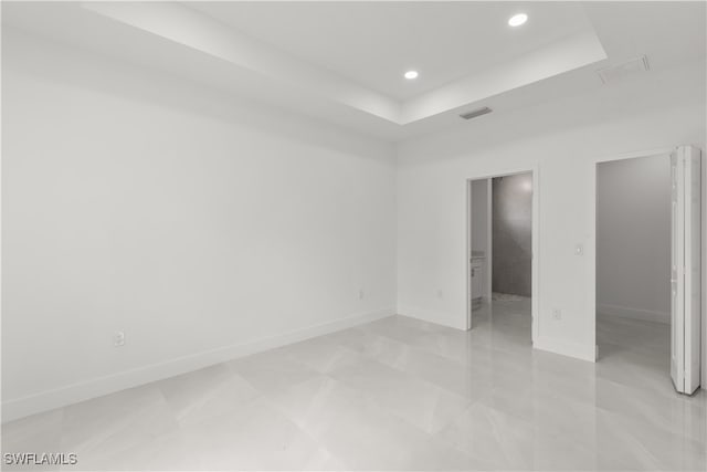 unfurnished bedroom featuring ensuite bath, a spacious closet, and a tray ceiling