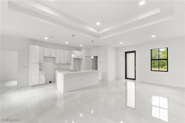 kitchen featuring white cabinetry, a center island with sink, sink, and hanging light fixtures