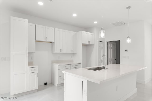 kitchen with a kitchen island with sink, white cabinetry, sink, light stone countertops, and hanging light fixtures