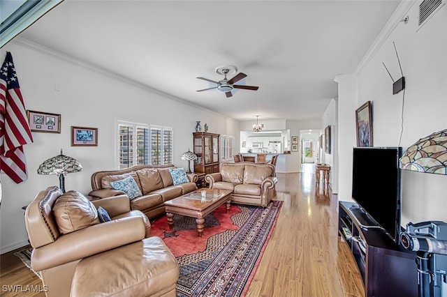 living room with ceiling fan with notable chandelier, light hardwood / wood-style floors, and crown molding