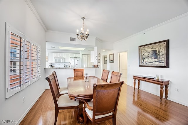 dining space with sink, ornamental molding, a chandelier, and light wood-type flooring