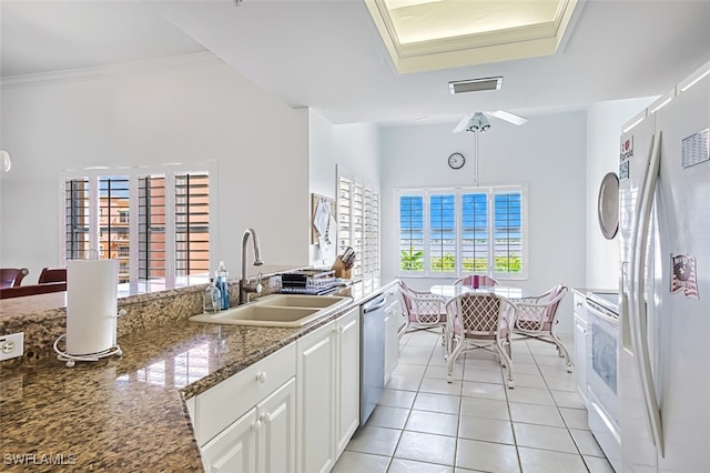 kitchen with dark stone counters, white appliances, sink, light tile patterned flooring, and white cabinetry