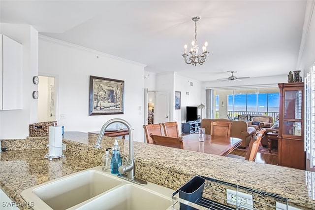 kitchen featuring crown molding, decorative light fixtures, sink, and light stone counters