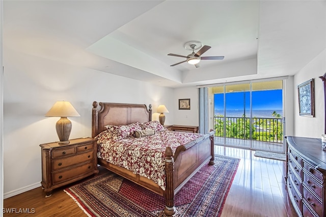 bedroom featuring wood-type flooring, a wall of windows, access to outside, a tray ceiling, and ceiling fan