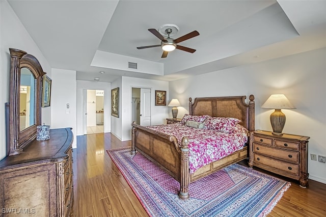 bedroom with a raised ceiling, wood-type flooring, ceiling fan, and ensuite bath