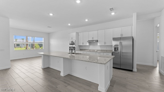 kitchen featuring light stone counters, appliances with stainless steel finishes, white cabinets, a center island with sink, and sink