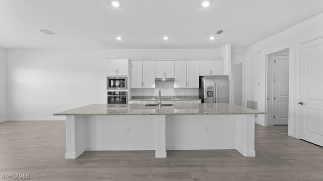 kitchen with white cabinetry, stainless steel appliances, a large island with sink, and light stone counters