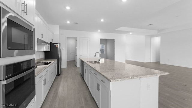 kitchen with a center island with sink, stainless steel appliances, light hardwood / wood-style floors, white cabinetry, and sink