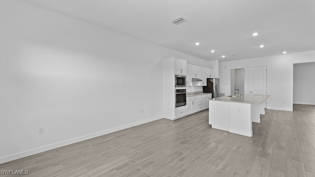 kitchen with light wood-type flooring, appliances with stainless steel finishes, an island with sink, and white cabinetry