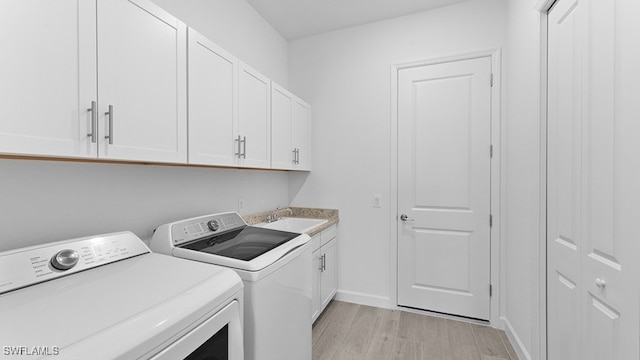 clothes washing area featuring light wood-type flooring, sink, cabinets, and washer and clothes dryer