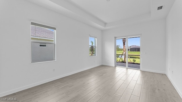 spare room with a raised ceiling and light hardwood / wood-style floors