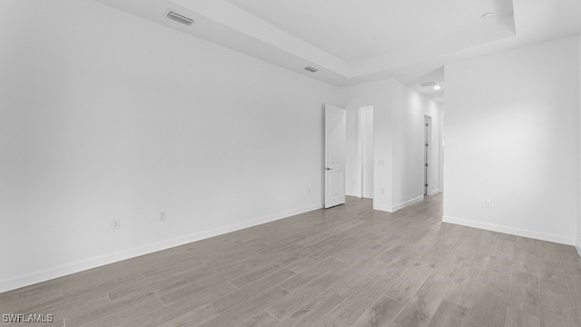 empty room with light wood-type flooring and a raised ceiling