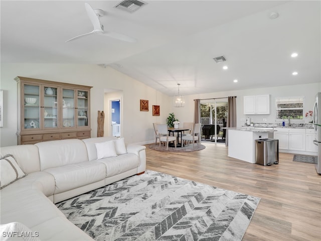 living room with sink, vaulted ceiling, light wood-type flooring, and ceiling fan with notable chandelier