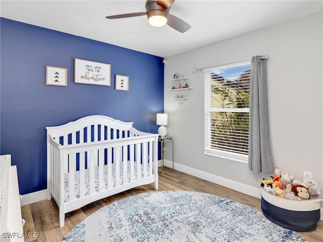 bedroom featuring ceiling fan, hardwood / wood-style flooring, and a nursery area