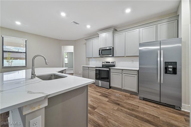 kitchen featuring gray cabinets, appliances with stainless steel finishes, sink, hardwood / wood-style flooring, and light stone countertops