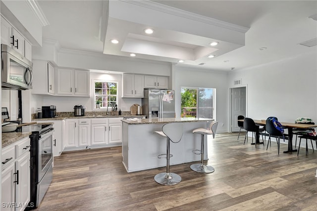 kitchen with white cabinetry, appliances with stainless steel finishes, a raised ceiling, hardwood / wood-style flooring, and a center island