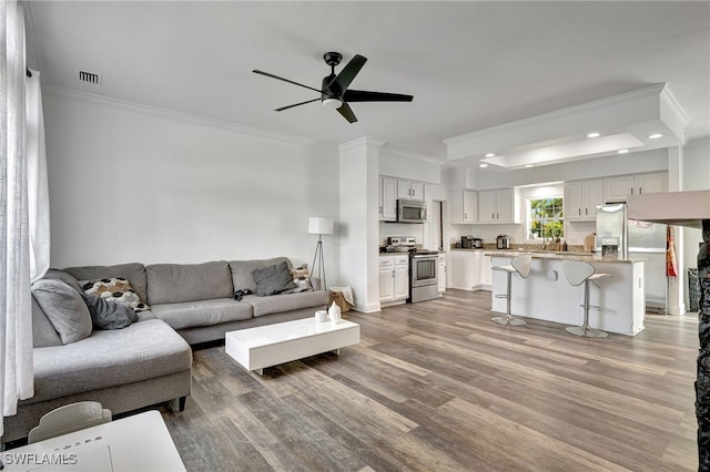 living room with ceiling fan, ornamental molding, and light hardwood / wood-style floors