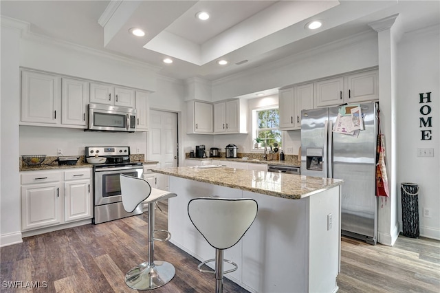 kitchen with dark wood-type flooring, stainless steel appliances, white cabinetry, and a kitchen island